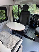 Cozy RV rental interior featuring a swivel driver's seat, dining table, and textured bench. Ideal for van life adventures.