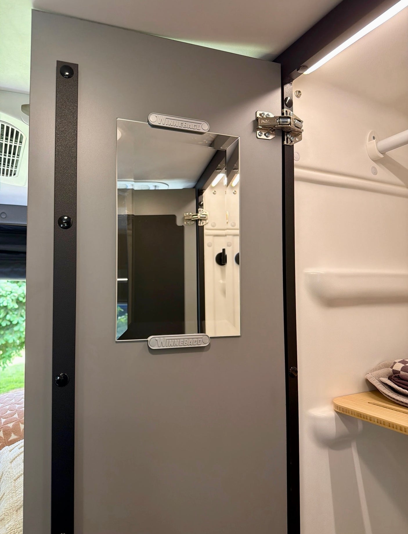 Winnebago rv rental: Grey door with mirror opens to a white interior, likely a shower or closet, with a wood shelf.