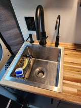 Modern RV rental interior: compact kitchen with stainless sink, black faucet, sponge & brush.