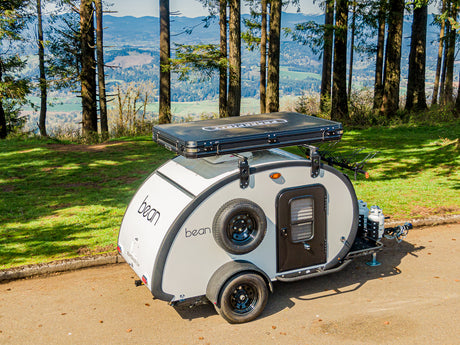 Bean teardrop trailer with rooftop tent, an ideal RV rental for camping adventures. Set in a forest with a scenic valley view.