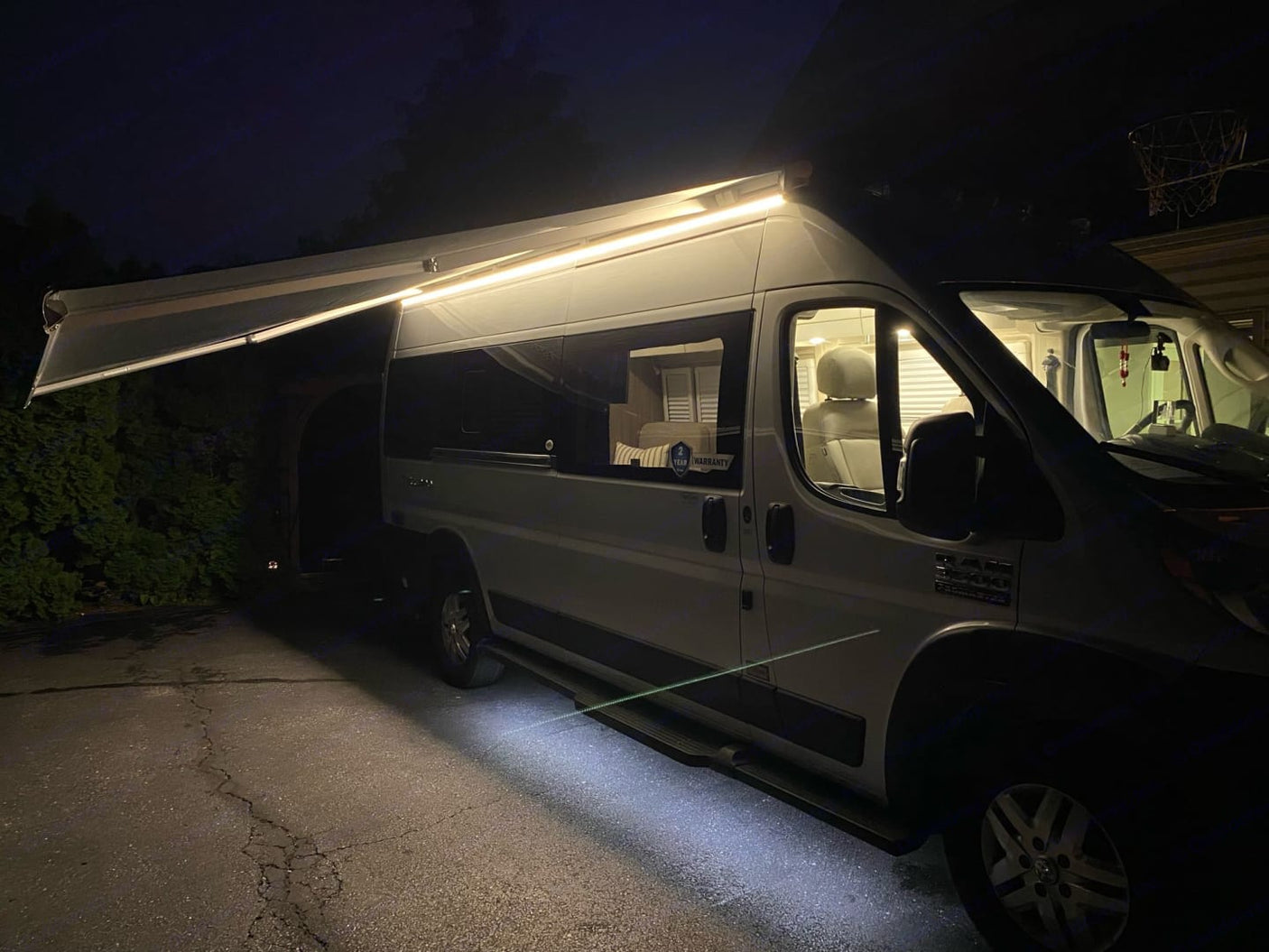 Night view of a white rv rental with its lighted awning extended. Bright lights illuminate the exterior and interior.