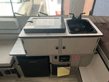 Compact kitchen & living space inside an RV rental, featuring a cooktop, sink, fridge, and cozy seating.