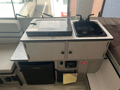 Compact kitchen & living space inside an RV rental, featuring a cooktop, sink, fridge, and cozy seating.