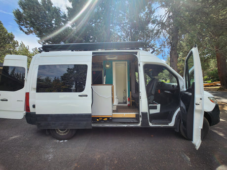 White Mercedes Sprinter camper van RV rental, doors open revealing a modern, fully equipped interior.