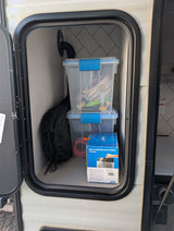 An RV rental's organized exterior storage, revealing clear bins with hoses, fittings, and a box of toilet waste bags.