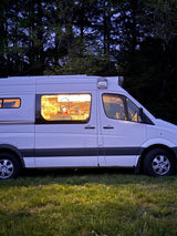 White RV rental camper van glowing at dusk, revealing a cozy interior kitchen & a dog in the front seat. Ideal for van life travel.
