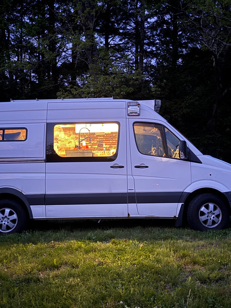White RV rental camper van glowing at dusk, revealing a cozy interior kitchen & a dog in the front seat. Ideal for van life travel.
