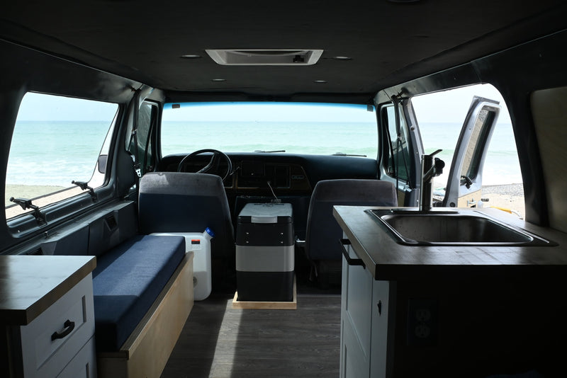 RV rental interior with ocean view: a custom camper van featuring a kitchen sink, fridge, and cozy bench by the sea. — photo 6