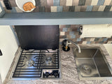 Compact RV rental kitchenette features a two-burner stove, stainless steel sink, and paper towel holder, ideal for camper cooking.