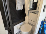 This RV rental wet bath features a compact toilet, shower curtain, mirror, and towels. Perfect for campervan adventures.