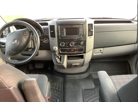 Explore the clean and spacious interior of this RV rental van, showcasing a modern Mercedes dashboard, steering wheel, and robust floor mats.