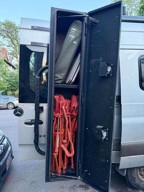RV rental Sprinter van's rear storage bay, neatly packed with a Camp Roll Table and several red folding chairs.
