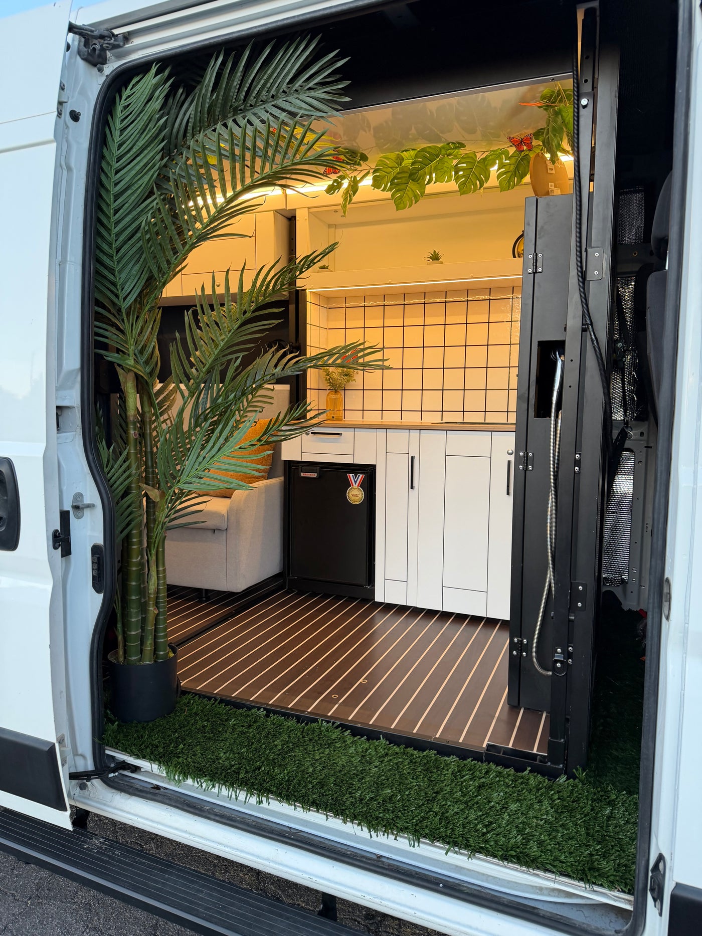 Entering an rv rental: features a modern kitchen, cozy sofa, and vibrant artificial plants, with an outdoor-like grass mat.