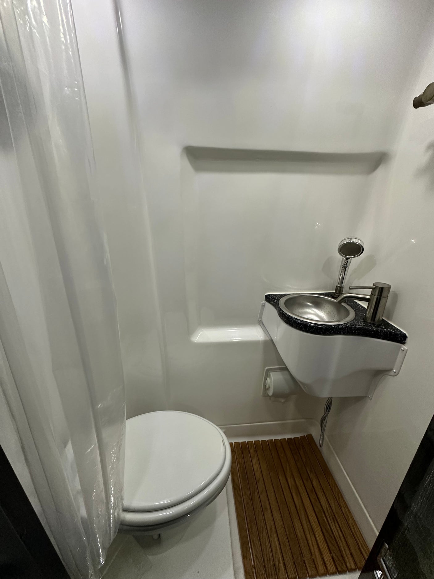 Compact RV rental wet bath with toilet, sink/shower combo, & wooden floor mat. Efficient design.