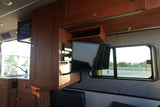 Inside this rv rental, wooden cabinets house a TV & microwave. A sink is visible, with a clear window view outside.