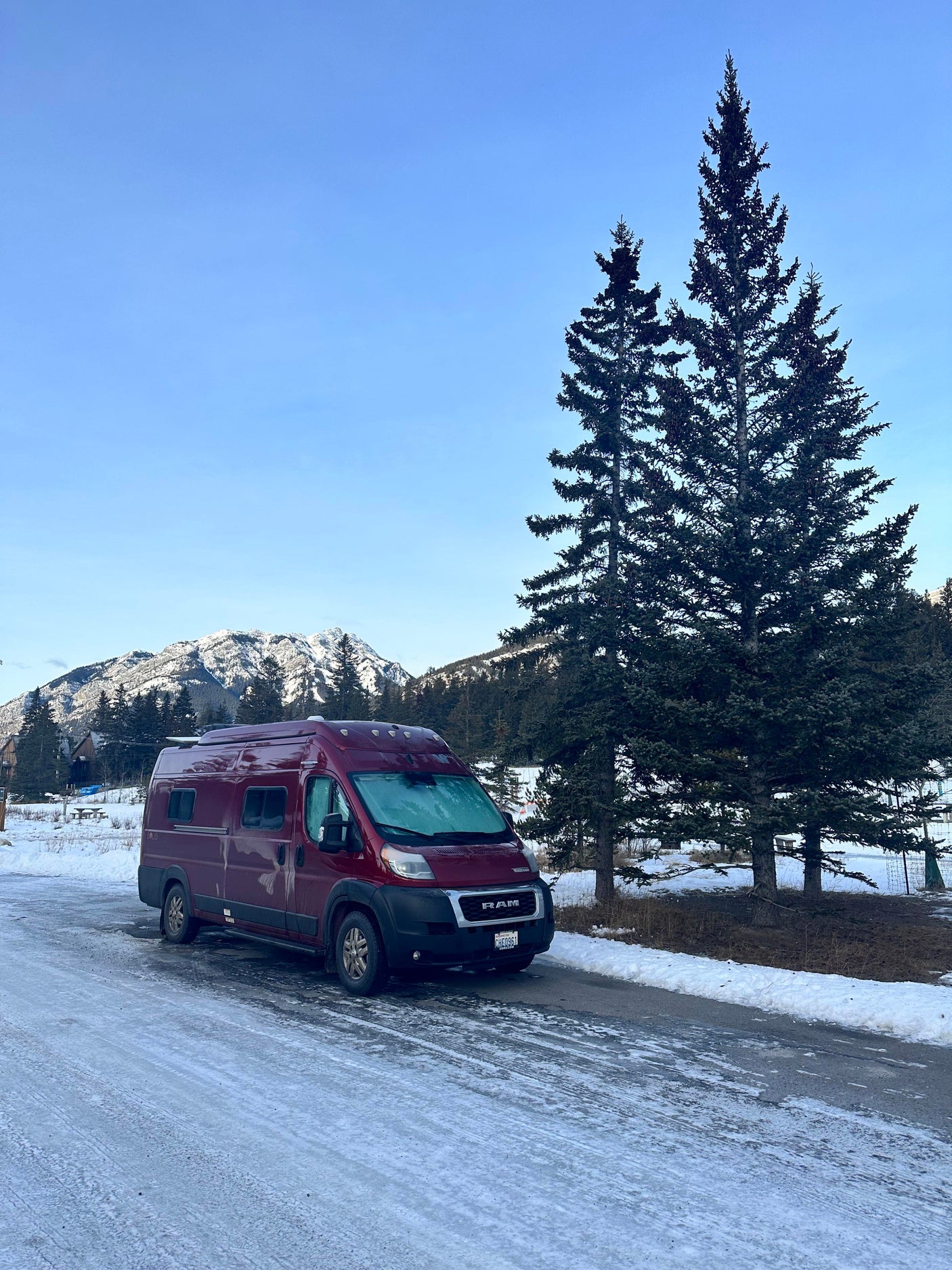 Red rv rental with frosted windshield parked on an icy road amidst snowy mountains and pines. Winter travel.