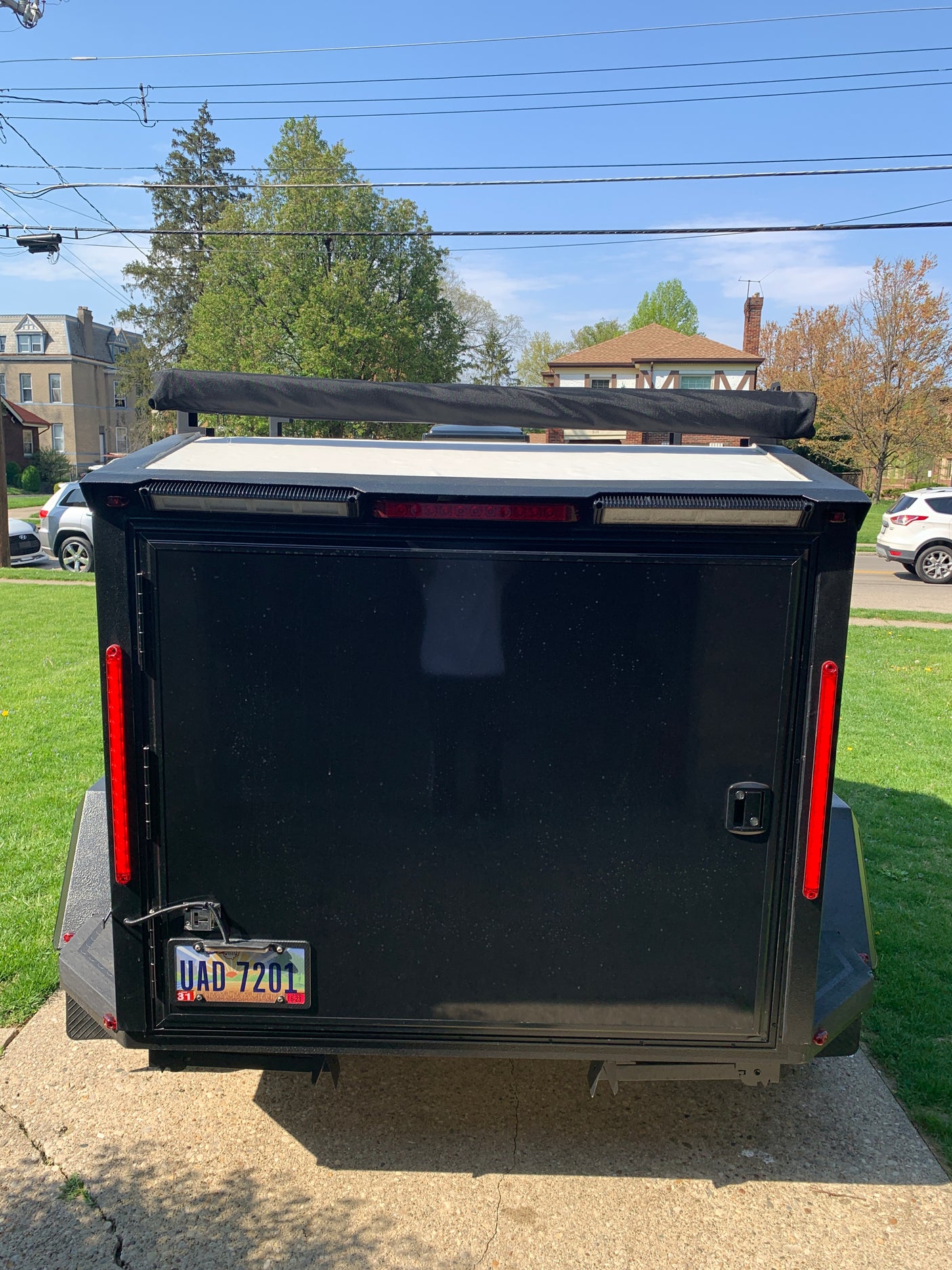Rear of black enclosed trailer, great for an RV rental trip, with license plate and awning. Parked on a sunny day.