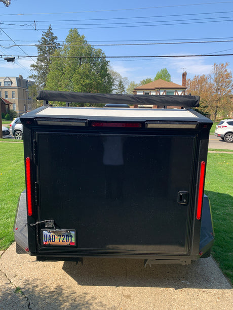 Rear of black enclosed trailer, great for an RV rental trip, with license plate and awning. Parked on a sunny day.
