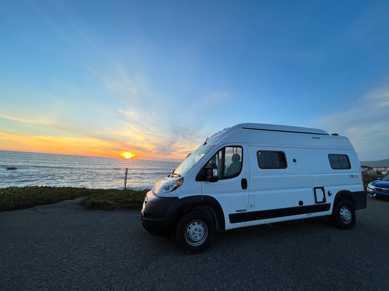 White Winnebago Solis RV rental parked oceanfront at sunset. Golden sun dips below horizon, waves crash on shore. Ideal for travel. — photo 2