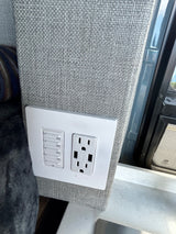 RV rental interior wall: grey fabric with a timer switch (10-60 min) and an electrical outlet featuring USB ports.