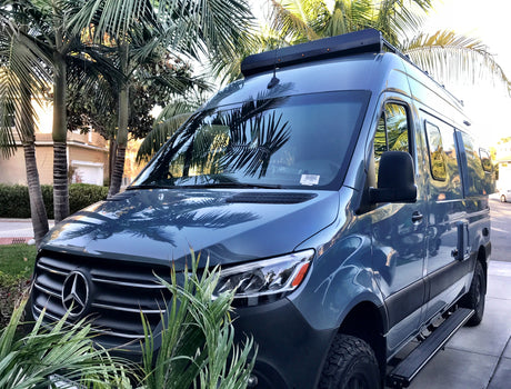 Modern blue Mercedes Sprinter RV rental parked among palm trees. Ready for your next adventure.