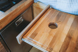 Space-saving pull-out wooden cutting board with a circular hole, perfect for food prep in this RV rental kitchen.