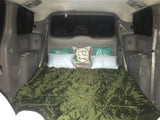 Cozy vehicle bed setup in a gray minivan/SUV, with a green sleeping bag and decorative pillows. Great for car camping or an RV rental experience.