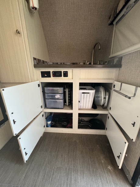 Inside an RV rental: a compact kitchen area with sink, counter, and open organized cabinets revealing storage solutions.
