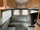 RV rental interior featuring light green leather seating, overhead wooden cabinets, and window blinds.