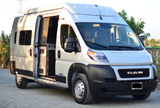 White Winnebago Ram ProMaster camper van RV rental with open side door revealing interior, parked on gravel.