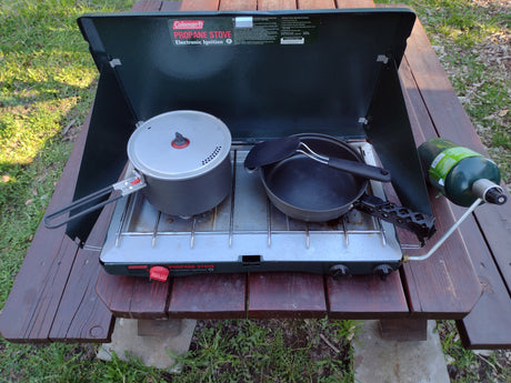 Coleman propane stove set on a picnic table, ready for outdoor cooking during your RV rental trip. Includes pots and propane tank.
