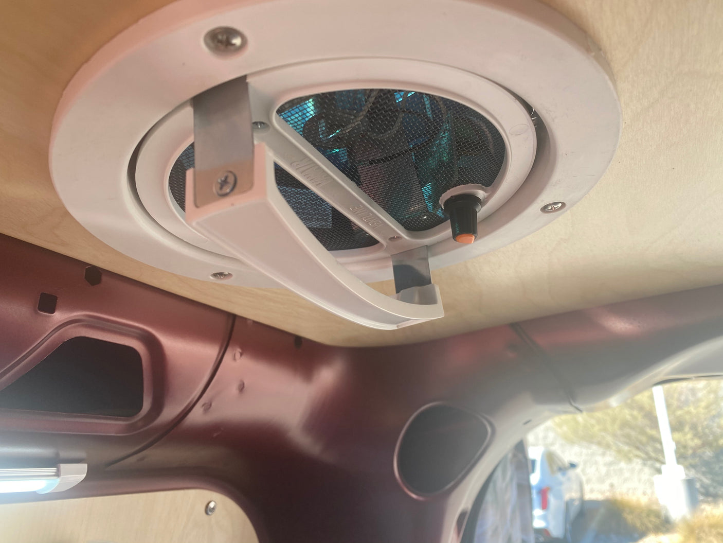 RV rental interior: Close-up of a white ceiling vent/fan with mesh, installed in a wooden panel for comfort and ventilation.