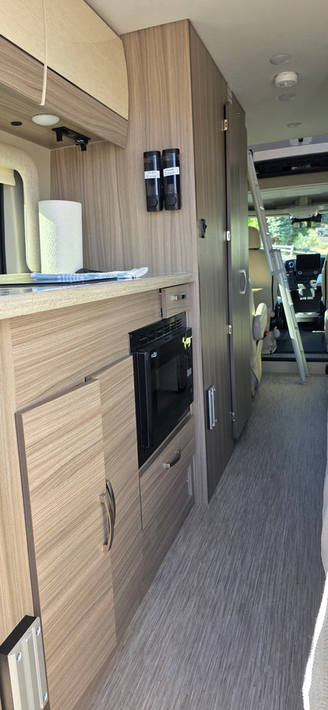 RV rental interior featuring a compact kitchen with microwave, cabinets, and soap dispensers for dish and hand wash.