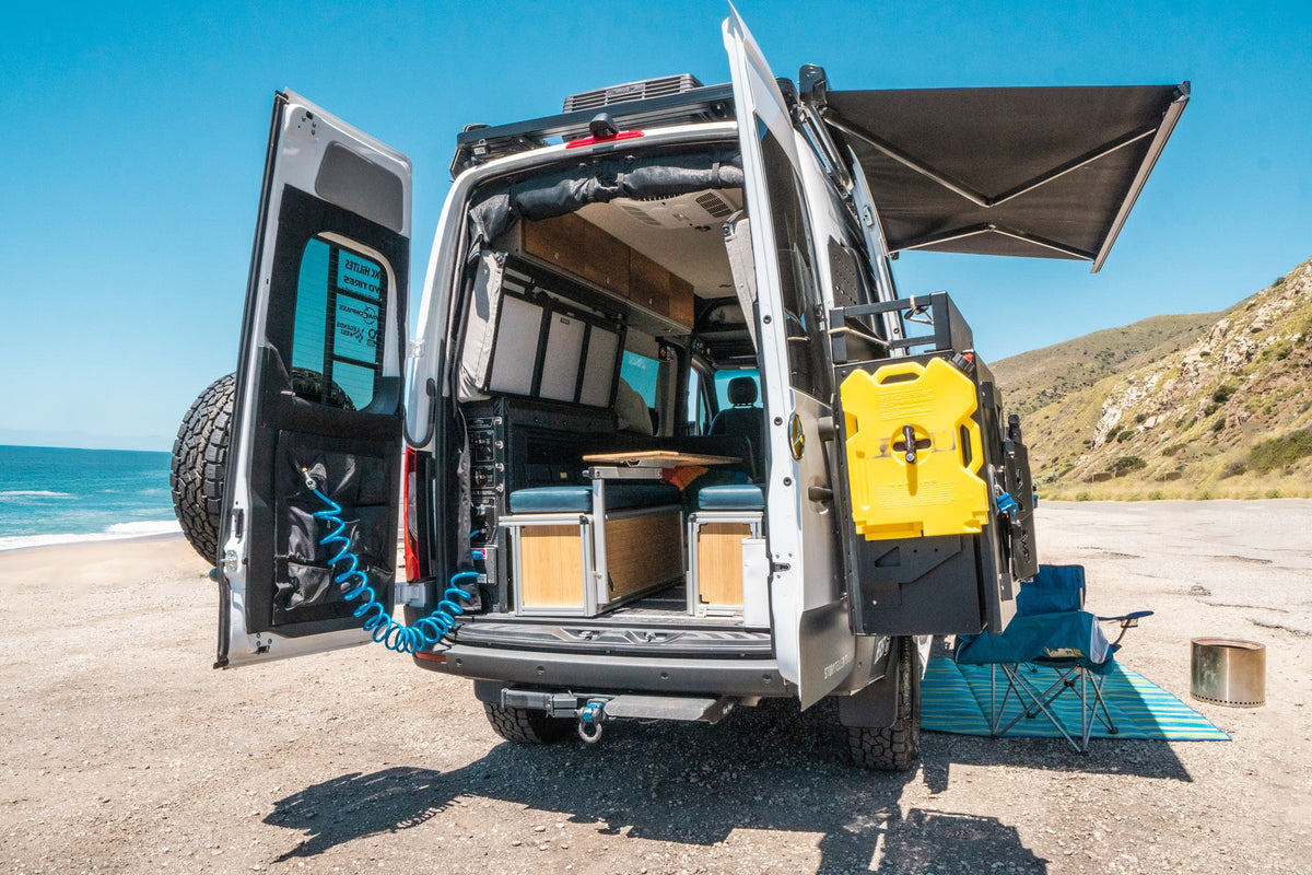 Rear view of an RV rental camper van at the beach, doors open revealing interior, water/fuel tank, and awning. — photo 2