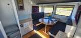 Bright RV rental interior featuring a dinette with blue and white seating, set table, and scenic windows.