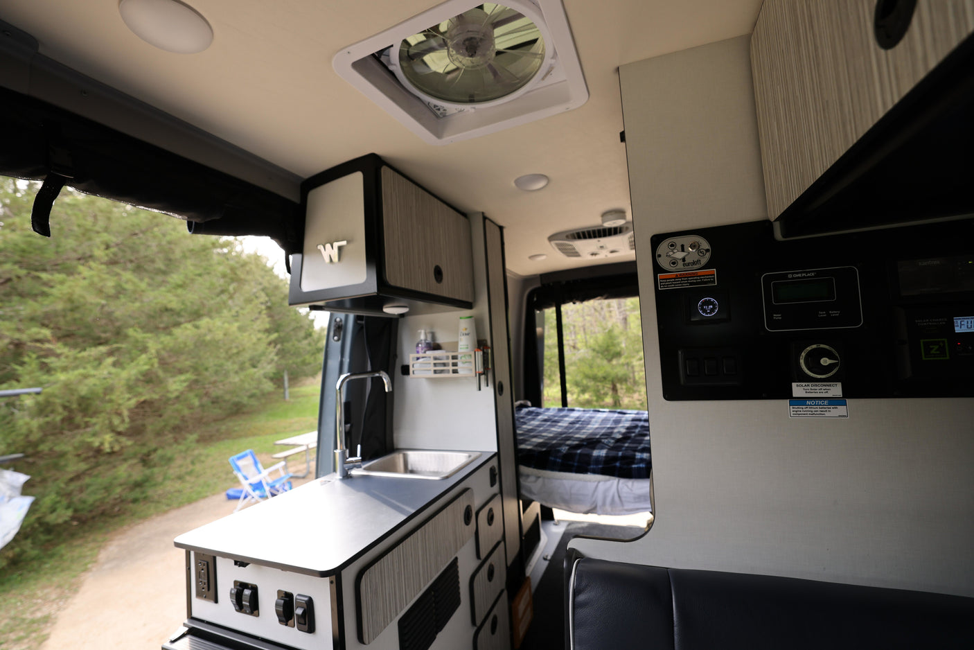 Spacious RV rental interior with kitchenette, solar controls, and a cozy bed, ready for outdoor adventures.