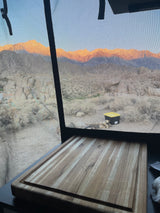 Golden hour in the desert from our RV rental. Stunning mountain views through a screen, with a cutting board inside.