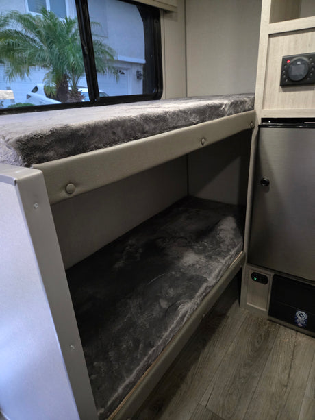 Cozy bunk beds with fuzzy gray mattresses inside an RV rental, featuring a window view, mini-fridge, and control panel.