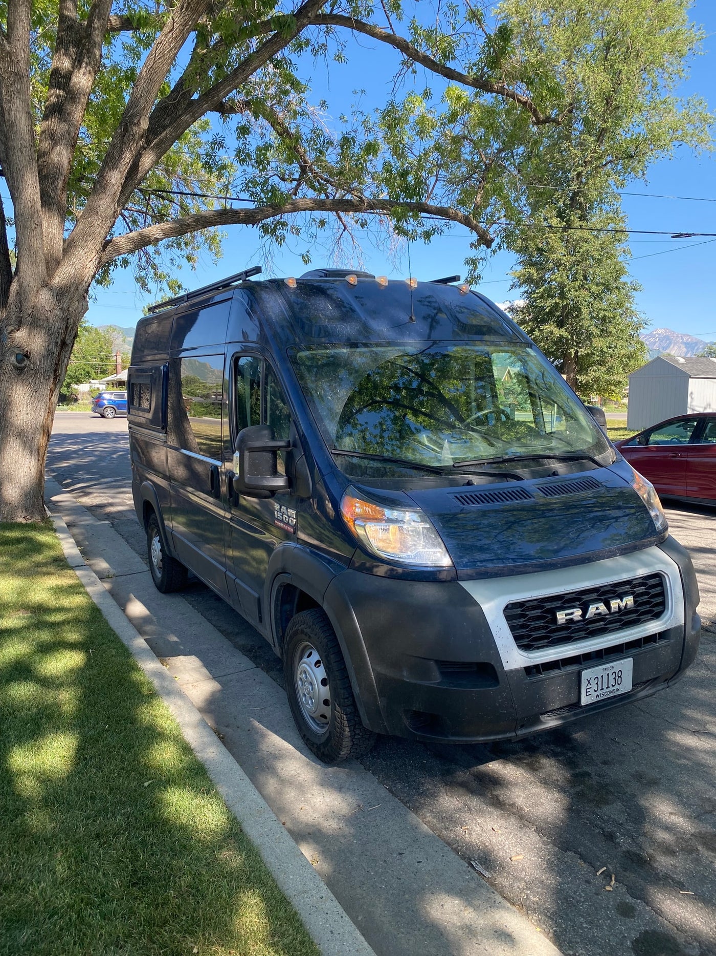 Dark Ram ProMaster campervan for rv rental, parked on a sunny street under a tree with mountains in the distance. — photo 13