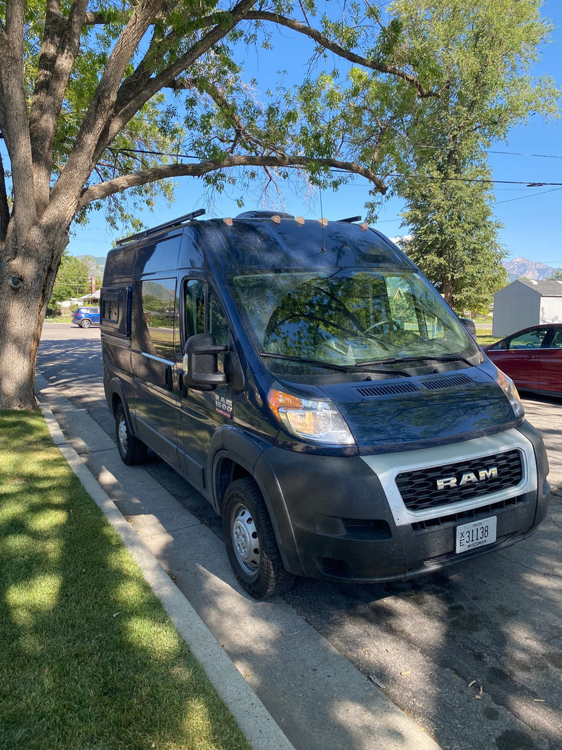 Dark Ram ProMaster campervan for rv rental, parked on a sunny street under a tree with mountains in the distance. — photo 13