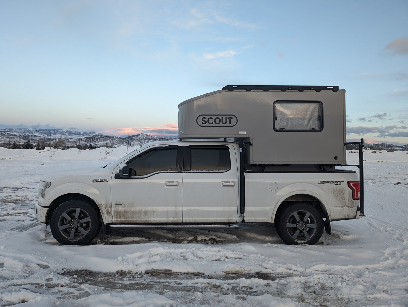 White pickup truck with a gray Scout truck camper, an ideal RV rental for snowy mountain adventures.