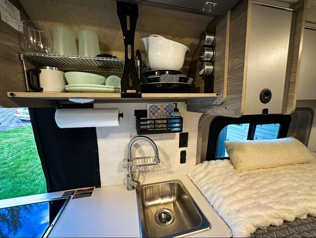 Inside an RV rental: a practical kitchen with sink, shelves, and spices, next to a plush bed. Everything needed for mobile living.