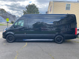 Black Sprinter van for rv rental parked on asphalt, reflecting houses & sky. Perfect for road trips & outdoor adventures.