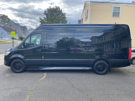 Black Sprinter van for rv rental parked on asphalt, reflecting houses & sky. Perfect for road trips & outdoor adventures.