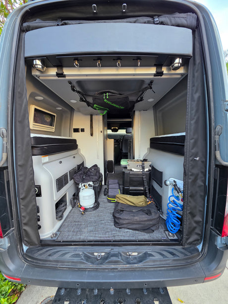 Packed RV rental camper van interior, featuring beds, camping stove, propane, and organized gear for trips.