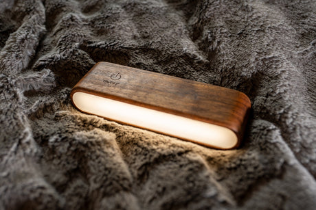 A glowing portable wooden lantern rests on a soft grey blanket, ideal for cozy evenings during an RV rental.