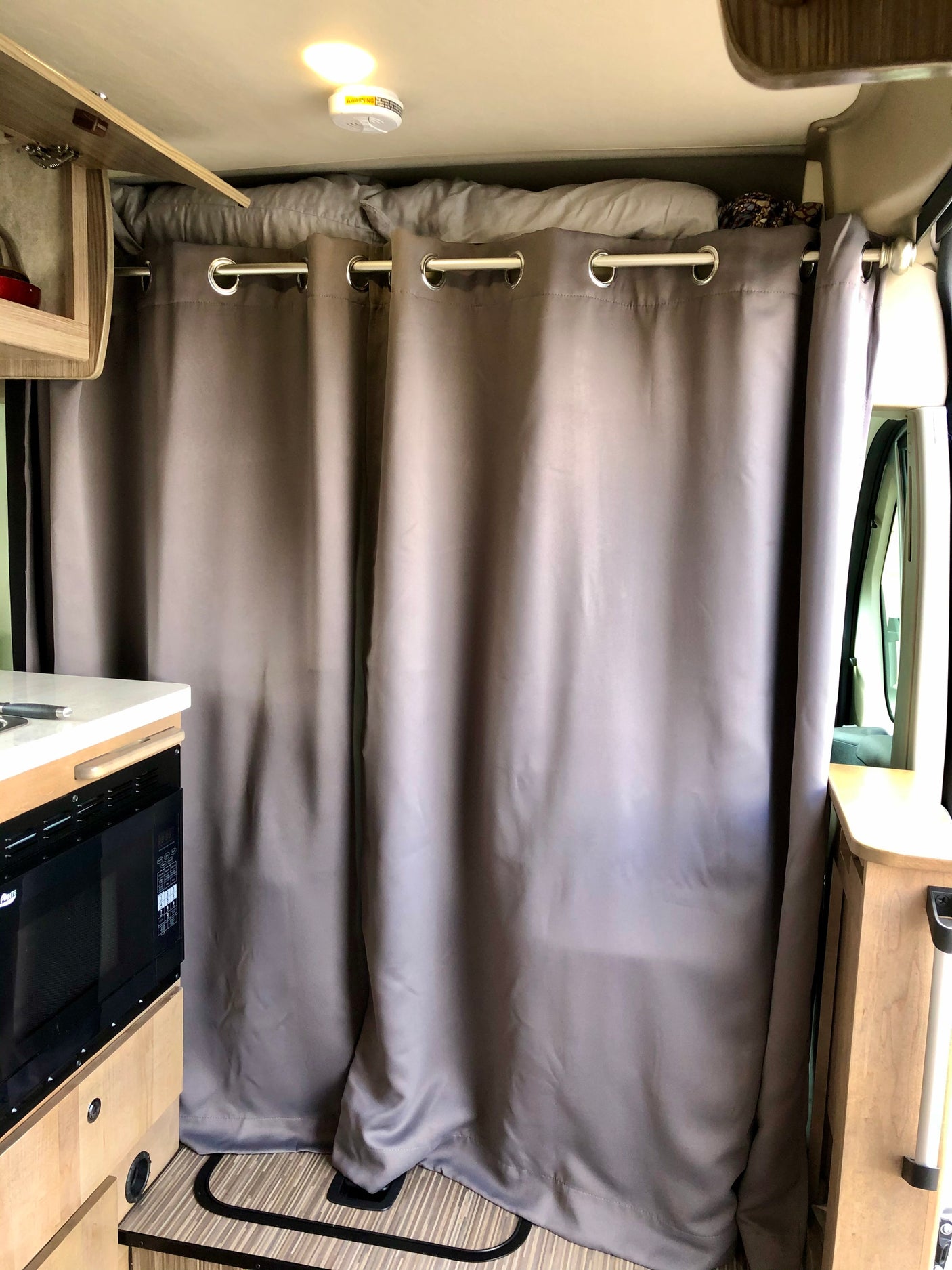 RV rental interior featuring privacy curtains, a compact kitchen with a microwave, and overhead bed storage.