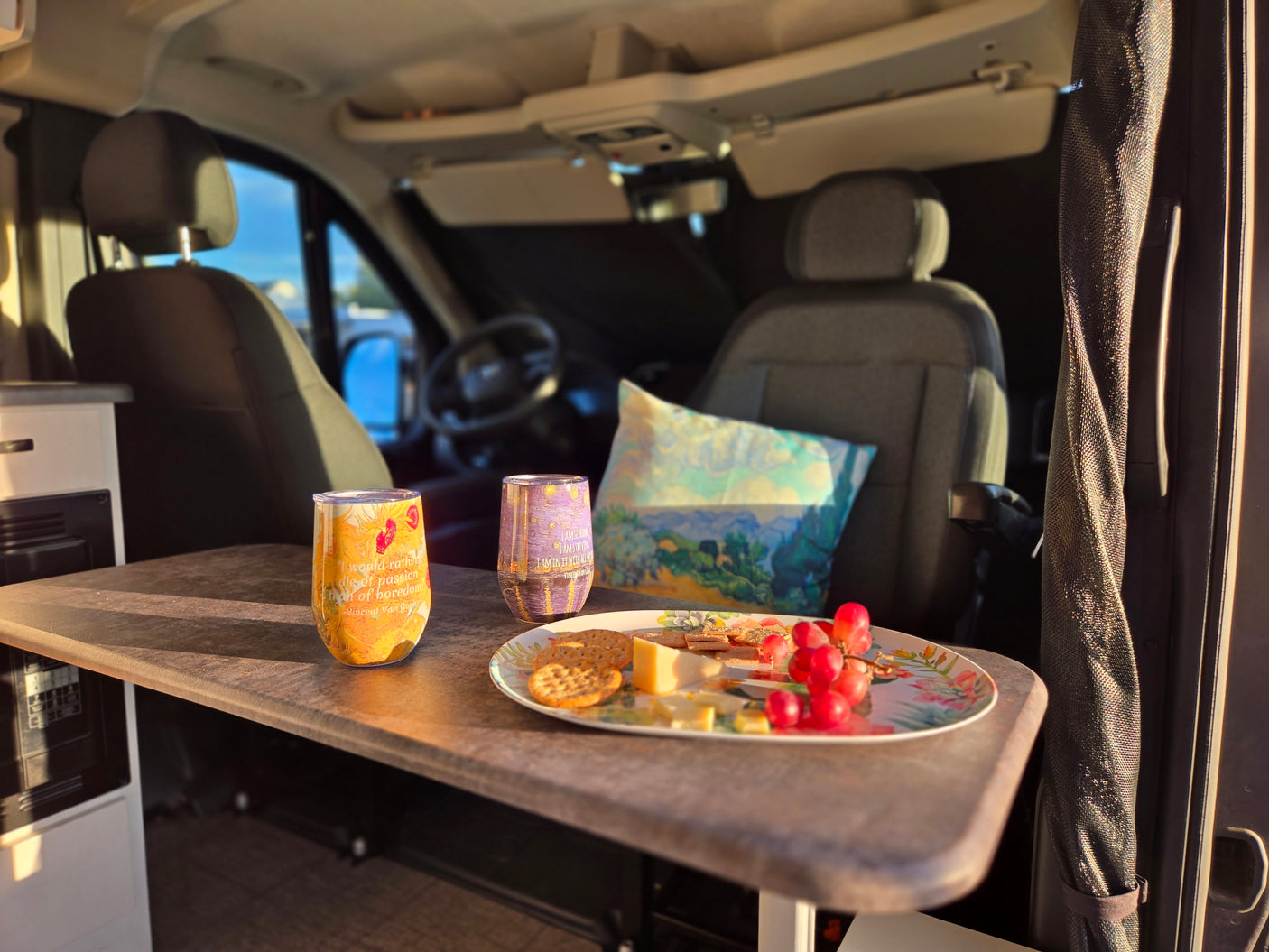 Relaxing in an RV rental: a table with cheese, crackers, grapes, and Van Gogh quote tumblers inside a cozy camper van.