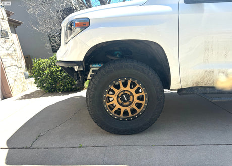White lifted pickup truck with bronze Method wheels, large off-road tires, and King shocks on a driveway.