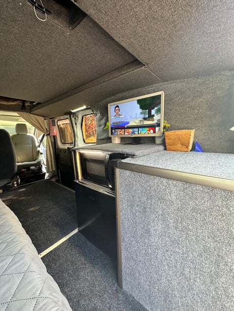 This RV rental's cozy van conversion features a TV, microwave, and gray carpeted interior for mobile comfort.